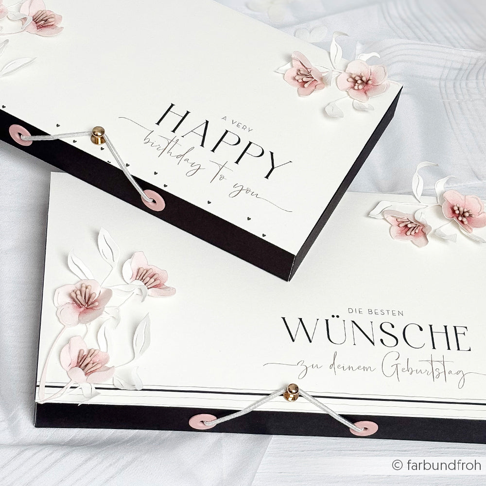 Zwei elegante, mit rosafarbenen Blumen verzierte Geburtstagskarten, die mit dem Alexandra Renke Motivstanze Quittenblüten Set ausgestanzt und mit zarten Kordelverschlüssen verziert wurden, präsentiert auf einer weißen Fläche.