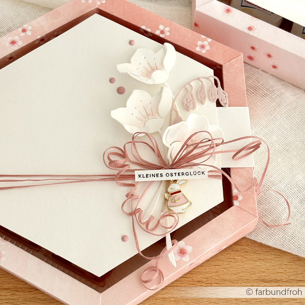 Sechseckige rosa Schachtel von Alexandra Renke, verziert mit Quittenblüten, rosa Schnur, Designpapier und einem kleinen Osterglockenanhänger.