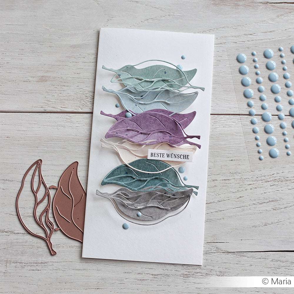 Handgemachte Karte mit geschichteten pastellfarbenen Papierblättern, blauen Punkten und einem "Beste Wünsche"-Aufkleber, hergestellt mit der Motivstanze Birnenblatt von Alexandra Renke und Stahlstempeln für präzises Design.