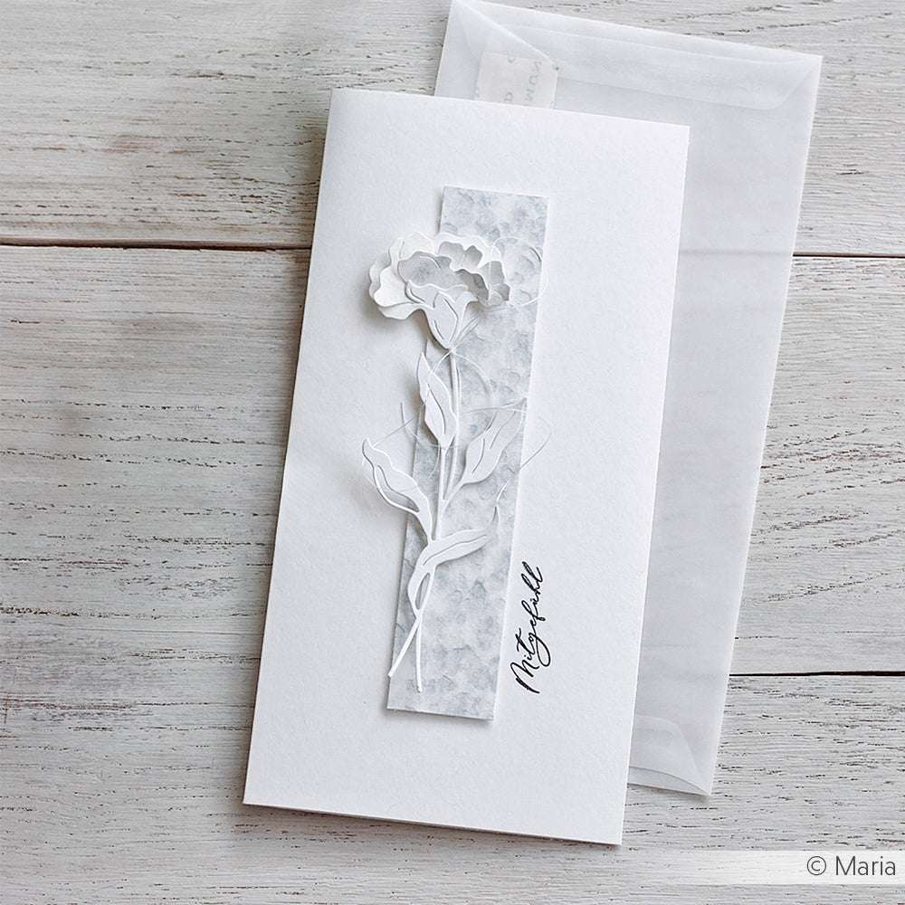 Eine weiße Karte von Alexandra Renke mit einer zarten Blume aus Schichtblume 12-Papier und dem Text "Mitgefühl" auf hellem Holz mit einem Umschlag - fachmännisch hergestellt mit Motivstanze Dies.