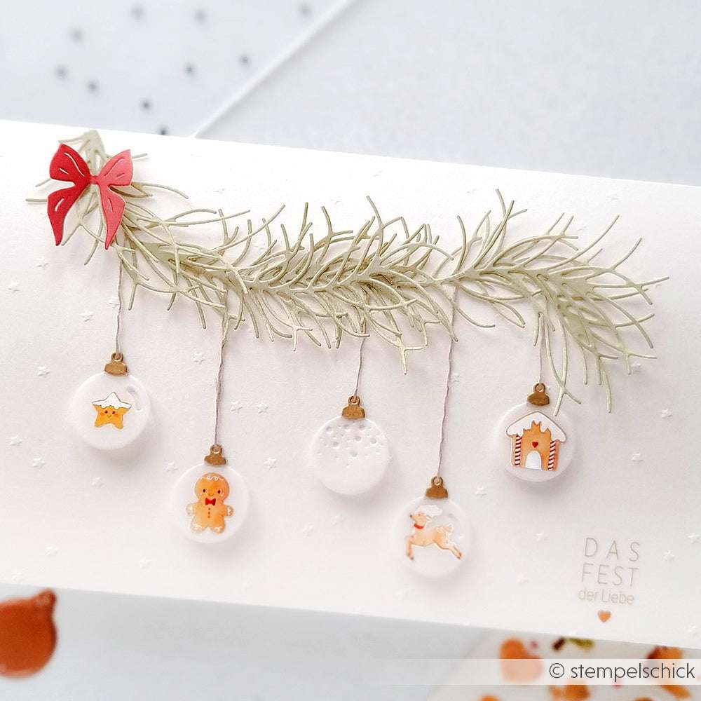 Eine weihnachtliche Karte von Alexandra Renke mit Ornamenten und Keksen, die an einem Tannenzweig hängen. Gestaltet mit der Motivstanze Tannenzweig und verziert mit einer roten Schleife.