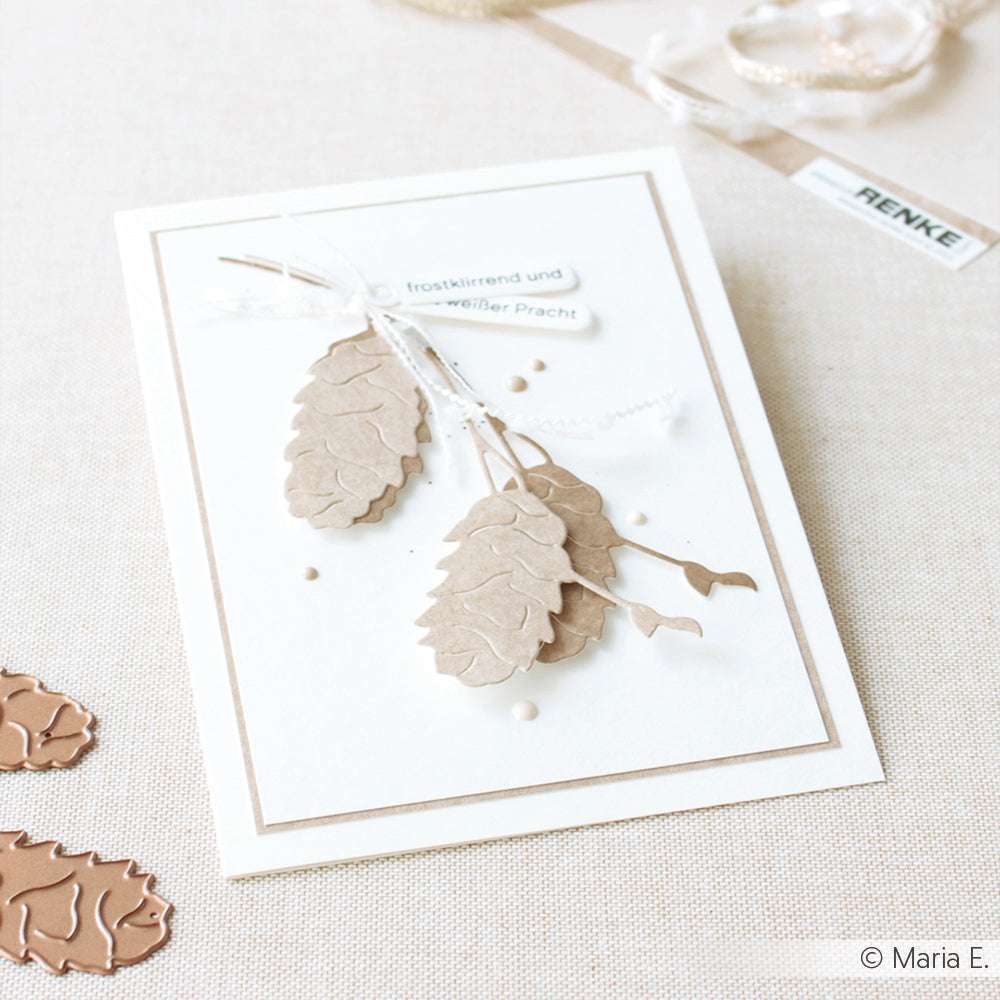 Handgemachte Karte mit geprägten braunen Tannenzapfen und Zweigen, hergestellt mit Alexandra Renke Motivstanze Längliche Tannenzapfen Dies, gebunden mit weißer Schnur auf beigem Hintergrund.