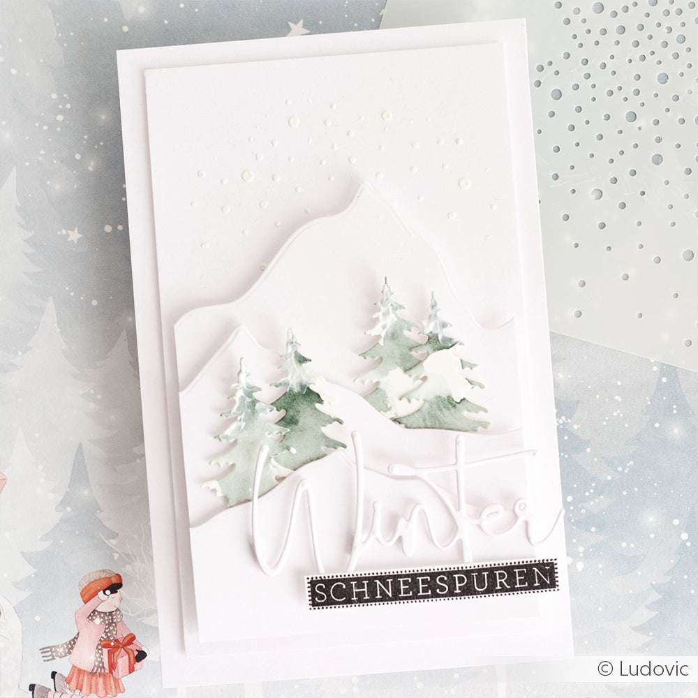 Handgemachte Karte von Alexandra Renke mit verschneiten Bergen, Tannenbäumen, die mit den Motivstanze Kleines Tannen-Duo Stanzformen hergestellt wurden, und den Worten Winter und Schneespuren auf weißem Hintergrund.