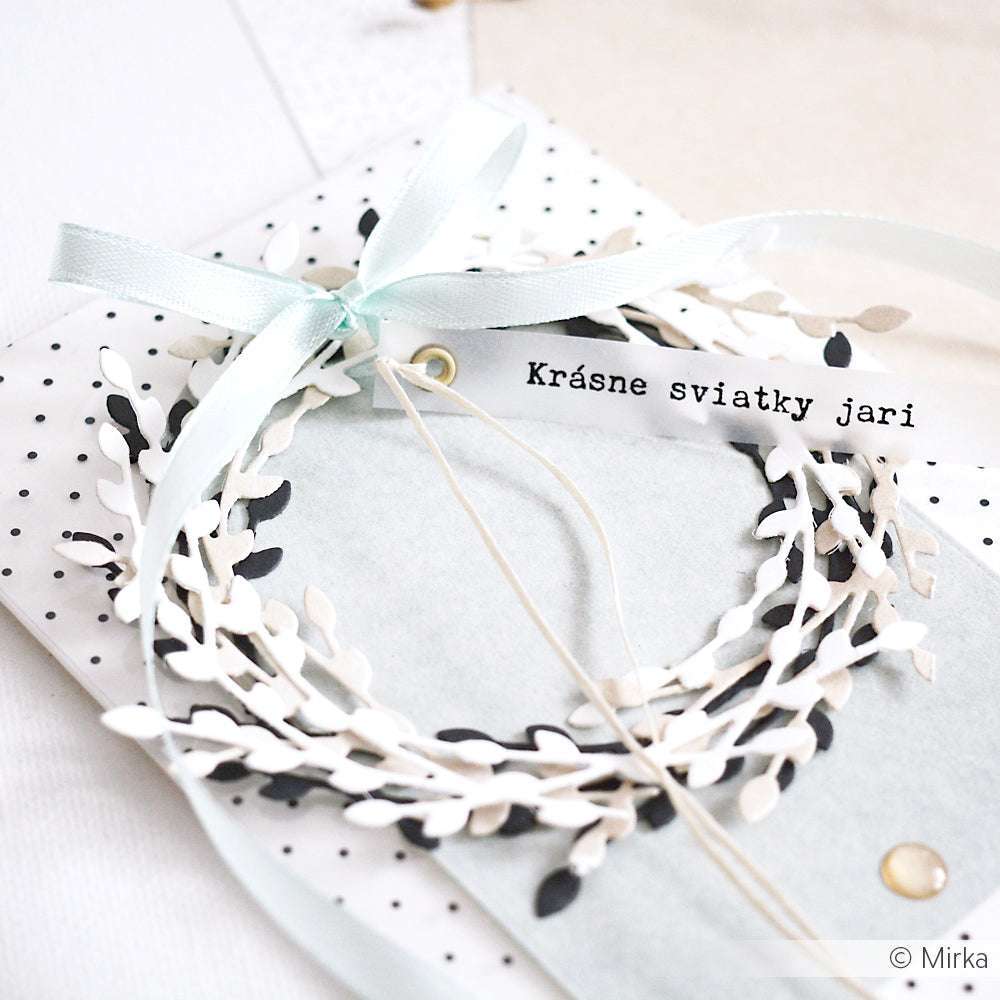 Auf einem gepunkteten Umschlag liegt ein weiß-schwarzer Papierkranz aus Alexandra Renke-Papieren und einem blauen Band mit der Aufschrift Krásne sviatky jari.