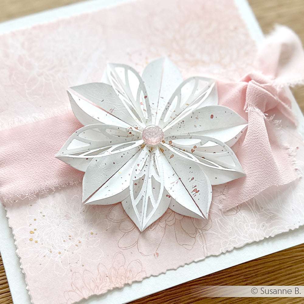 Handgefertigte Karte von Alexandra Renke mit weißer Motivstanze Faltblume auf rosafarbenem, strukturiertem Hintergrund, verziert mit einem zartrosa Band. Gefertigt mit hochwertigen Designpapieren 200g für eine elegante Note.