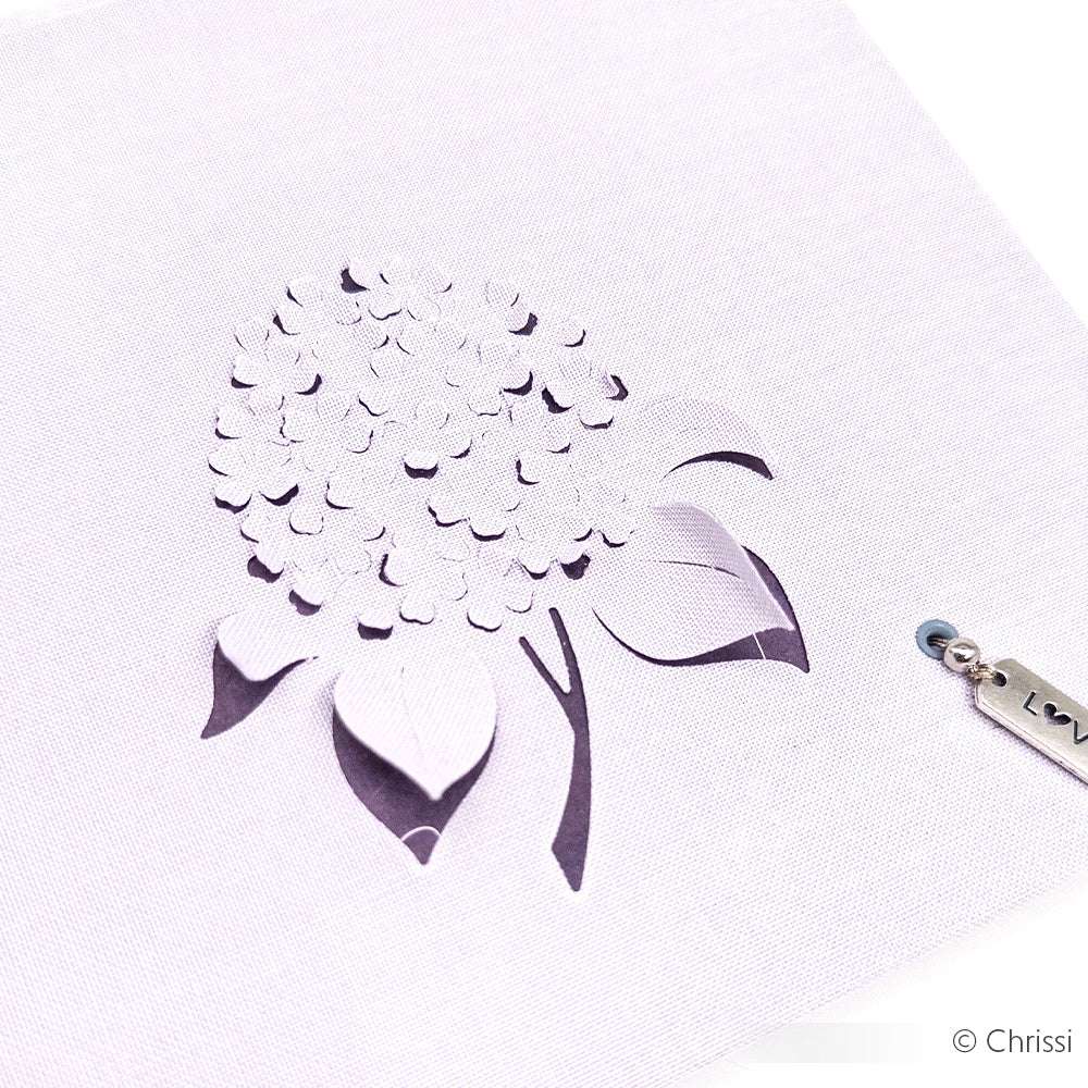 ☆ weißes Papier mit einem ausgeschnittenen Blumenmuster und einem kleinen Metallanhänger unten rechts - perfekt für Buchbinden-Projekte und aus FSC-zertifizierten Materialien hergestellt.