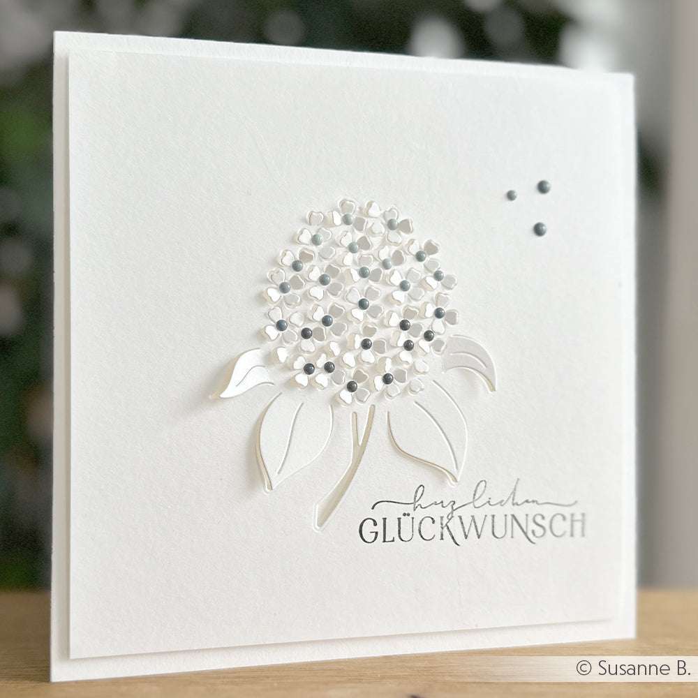 Handgefertigte weiße Karte von Alexandra Renke mit einem zarten Blumenmotiv aus der Motivstanze Negativ-Blume und dem deutschen Text "Herzlichen Glückwunsch".