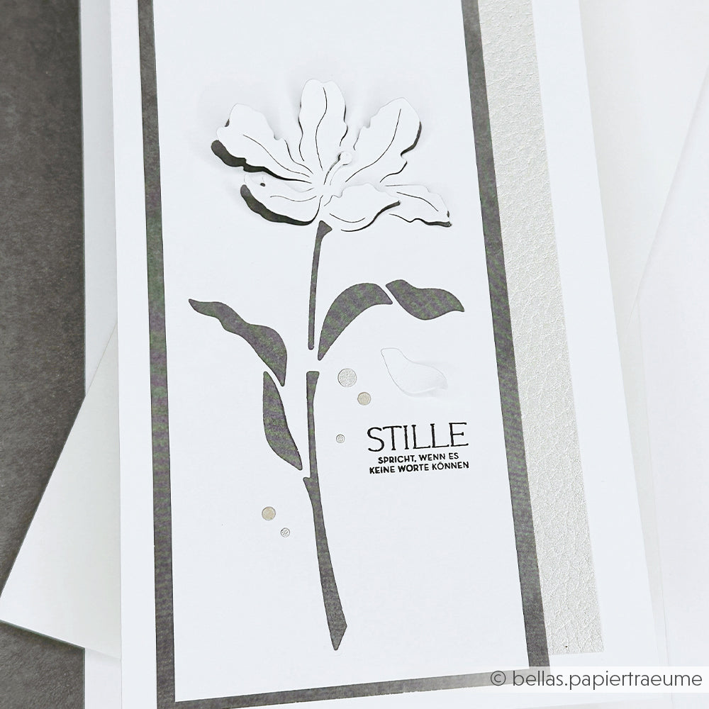 Weiße Blumenkarte mit geschichteten Blüten und Blättern, mit deutschem Text auf grau-weißem Hintergrund. Hergestellt mit Alexandra Renke Designpapieren und Motivstanze Negativ-Blume 5 für elegante Details.