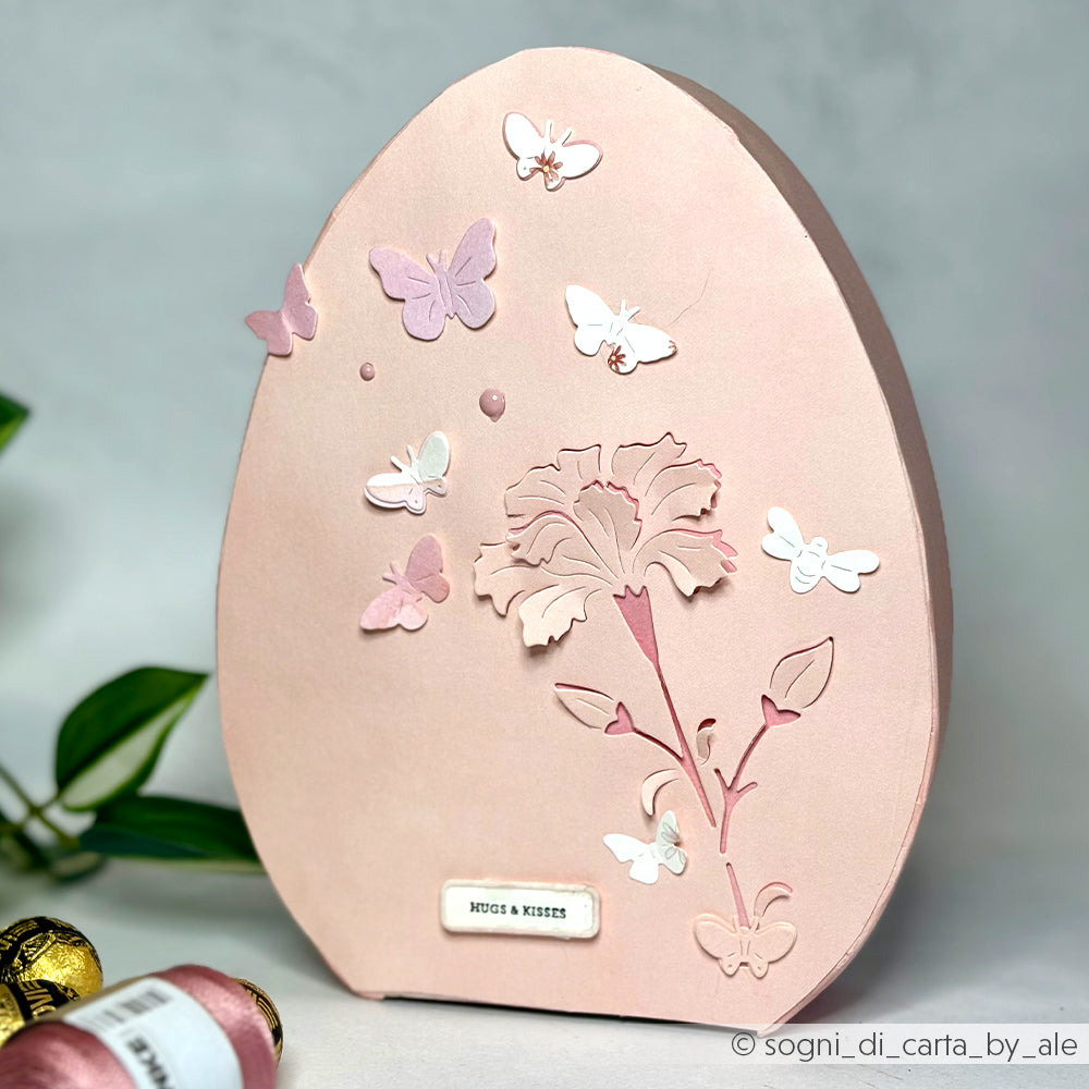 Rosafarbene Karte in Eiform mit Schmetterlingen und Blumenmotiv, hergestellt mit Alexandra Renke Dies für Papierbasteln, mit der Motivstanze Negativ-Blume 6 und einem kleinen Etikett "HUGS & KISSES" am unteren Rand.