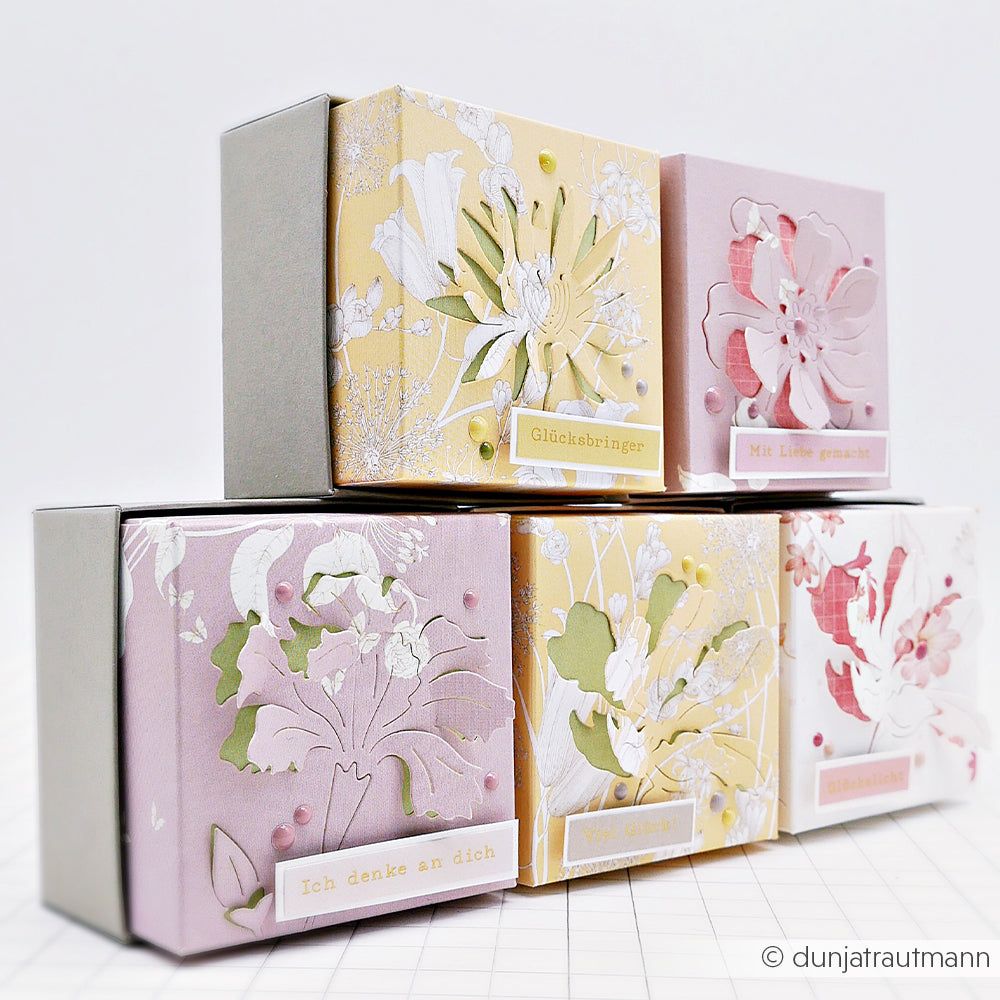 Fünf dekorative pastellfarbene Geschenkboxen mit floralen Motiven von Alexandra Renke, hergestellt mit DieCut Systemen und Designpapieren, sind in zwei Reihen auf einer weißen Fläche gestapelt.