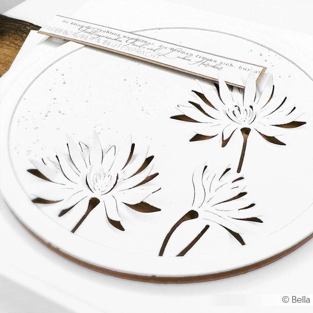 Weißes, rundes Designpapier von Alexandra Renke mit drei ausgeschnittenen Blumenmotiven aus der Motivstanze Negativ-Blume 7 und einer handschriftlichen Notiz am Rand.