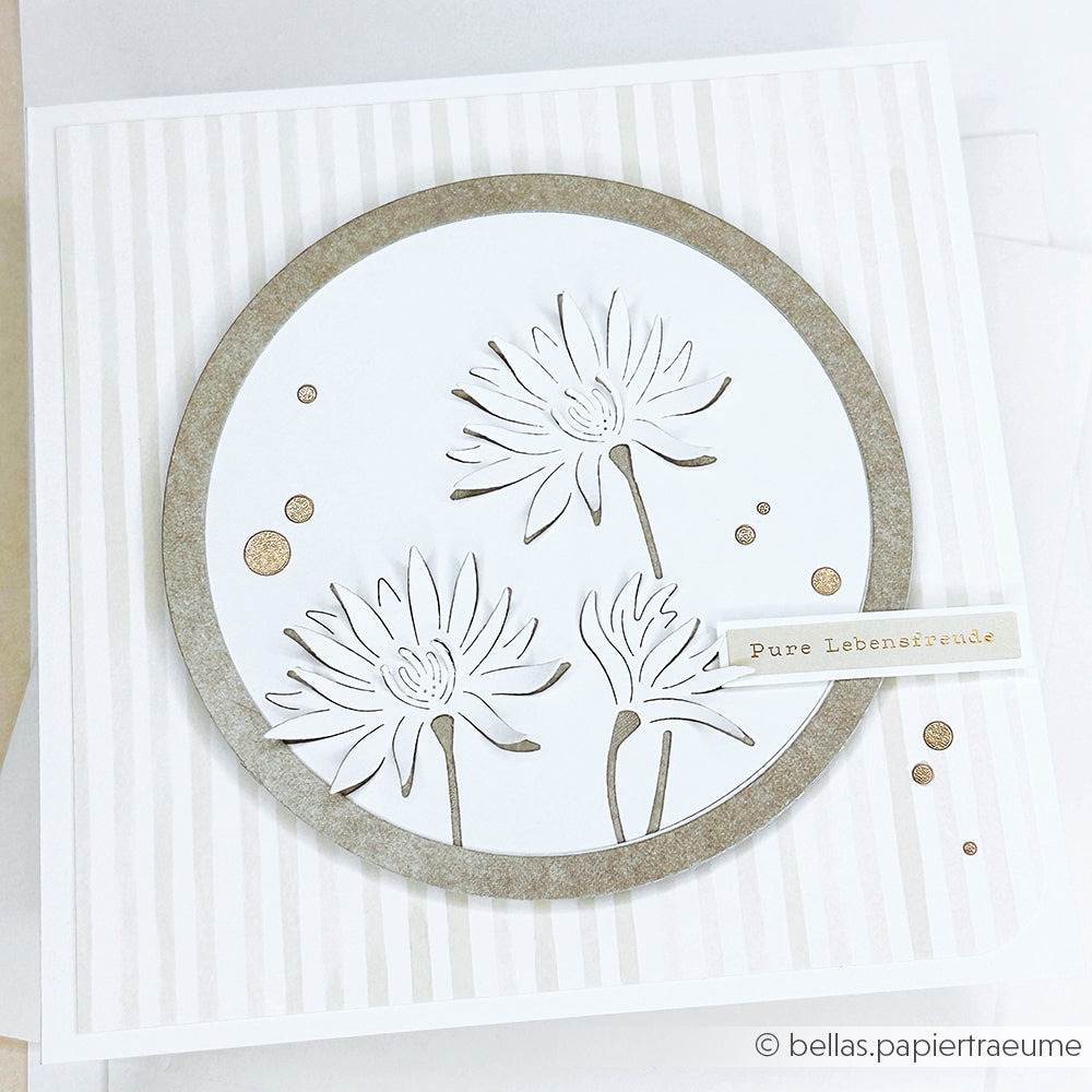Handgefertigte Karte von Alexandra Renke aus Designpapier mit drei weißen Blumen mit Goldrand, die mit der Motivstanze Negativ-Blume 7 DieCut Systeme geschnitten wurden, und einem Anhänger "Pure Lebensfreude" auf der rechten Seite.