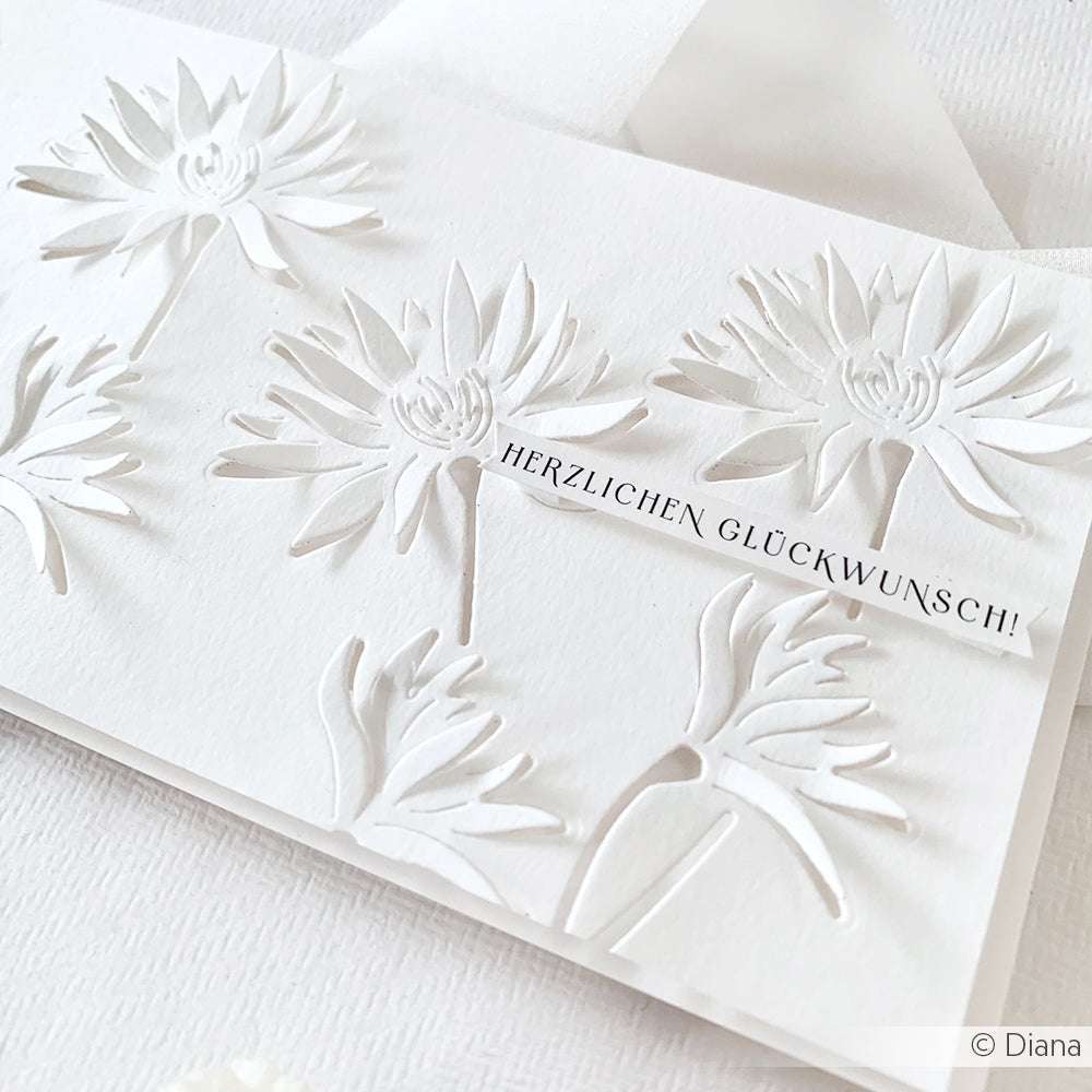 Weiße Karte mit filigranen Blumenausschnitten, hergestellt mit Alexandra Renke DieCut Systeme & Motivstanze Negativ-Blume 7, veredelt mit einem "HERZLICHEN GLÜCKWUNSCH!"-Etikett.