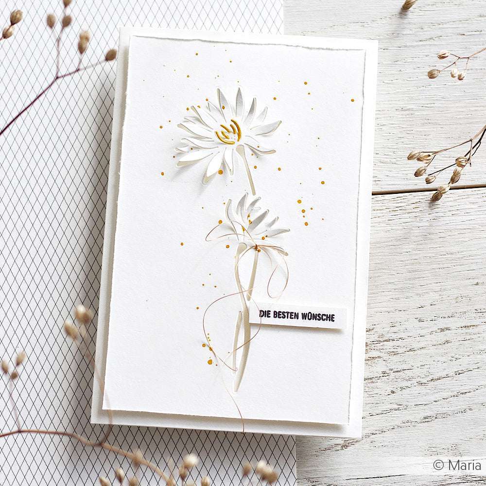 Weiße Grußkarte mit zwei Gänseblümchen aus Alexandra Renke Motivstanze Negativ-Blume 7, Goldspritzern und "DIE BESTEN WÜNSCHE" auf einer weißen Holzoberfläche - perfekt zum Basteln mit Alexandra Renke Stanzsystemen und Designpapieren.