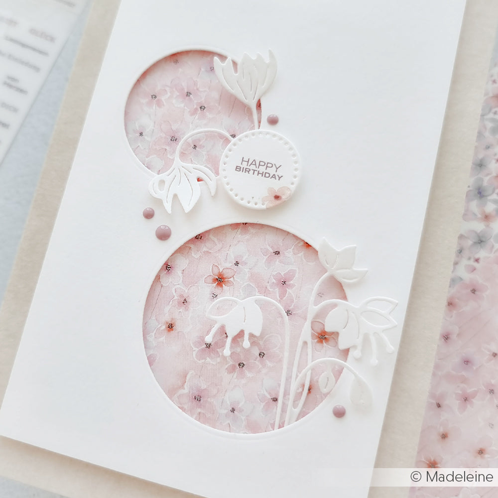 Weiße Geburtstagskarte von Alexandra Renke mit floralen Ausschnitten, gestaltet mit Stanzsystemen und Designpapieren, mit einem rosa Kirschblütenhintergrund und zarten Verzierungen.