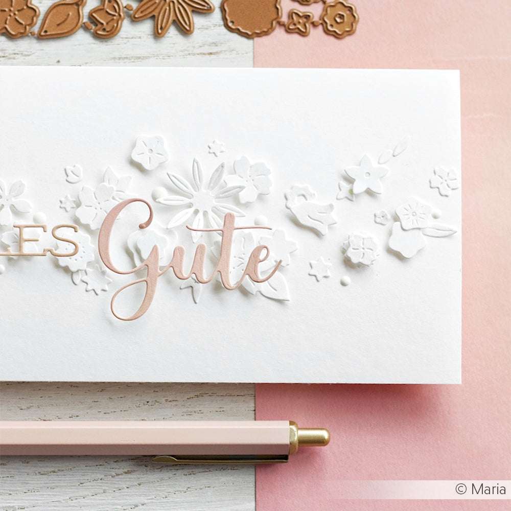 Weiße Karte mit erhabenen weißen Blumenmustern, hergestellt mit Alexandra Renke Stanzsysteme und "Gute" in Metallic-Schrift, daneben ein rosa Stift auf einer rosa Fläche.