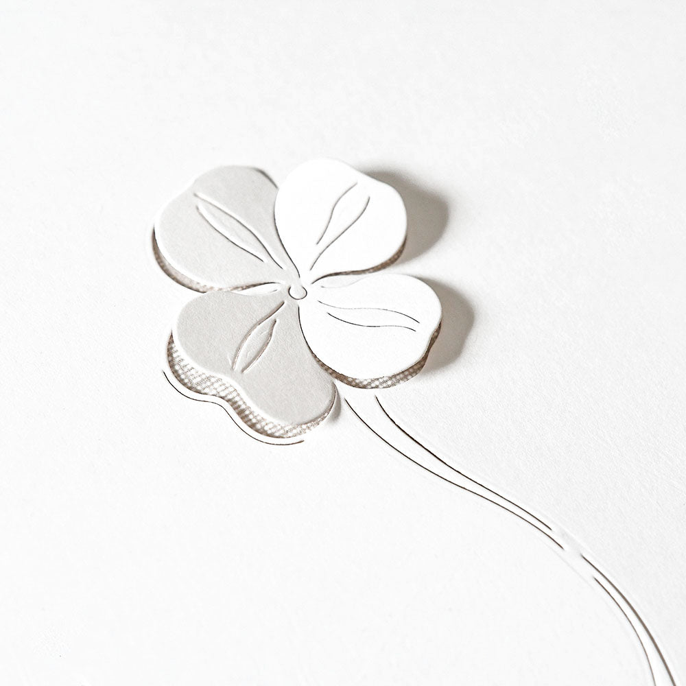 Weißer Papierausschnitt eines vierblättrigen Kleeblatts, hergestellt mit Alexandra Renke Stanzformen, mit zarten Linien auf einem einfachen weißen Hintergrund.