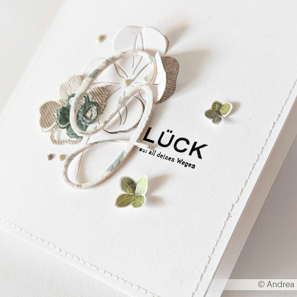 Handgemachte Karte von Alexandra Renke mit geschichteten Papierblumen, grünen Blättern und "GLÜCK" auf weißem Cardstock, hergestellt mit Designpapieren und DieCut Systemen für einen eleganten Touch.