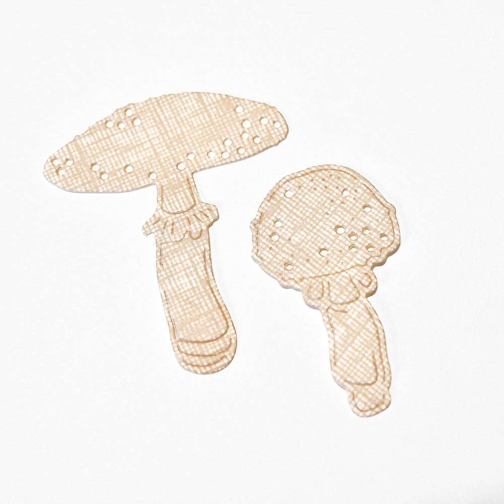 Zwei beigefarbene, pilzförmige Binden mit kleinen Löchern, inspiriert von Alexandra Renke's Motivstanze Glückspilz Duo DieCut Systeme, sind auf einem weißen Hintergrund platziert.