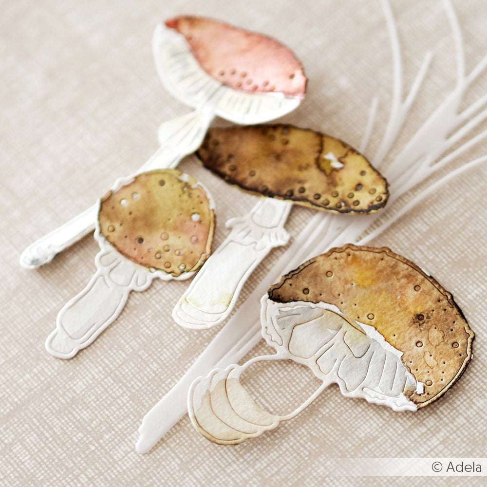 Aquarell-Illustration von drei Pilzen mit braunen und rosa Kappen auf einem leicht strukturierten Hintergrund, inspiriert von den skurrilen Formen der Alexandra Renke Glückspilz Duo 2 Stanzformen.