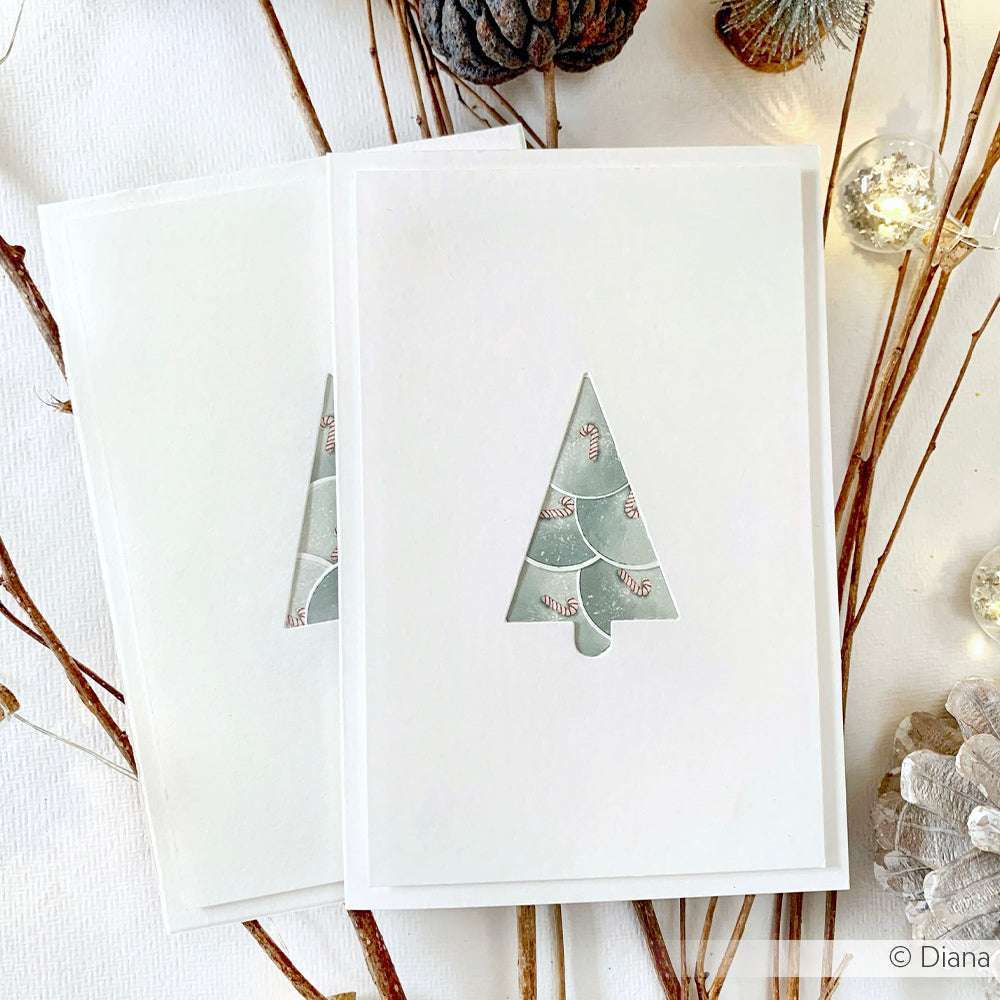 Minimalistische Weihnachtskarten von Alexandra Renke, hergestellt auf elegantem Designpapier mit einem ausgeschnittenen Baummotiv, verziert mit natürlichem Winterschmuck und Zweigen.