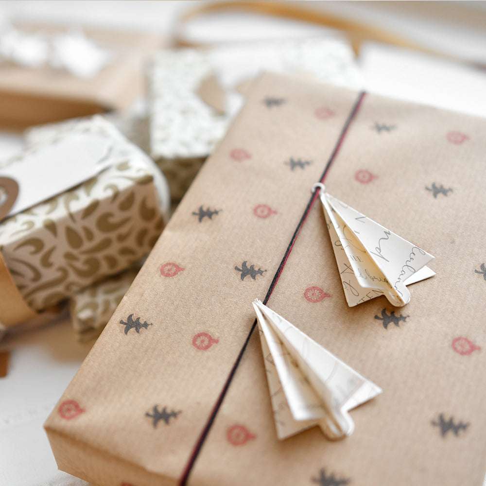 In braunes Papier eingewickeltes Geschenk mit Origami-Flugzeugen aus Alexandra Renke Stanzen für Designpapier, umgeben von anderen Geschenken, die mit Alexandra Renke DieCut Systemen verziert sind.