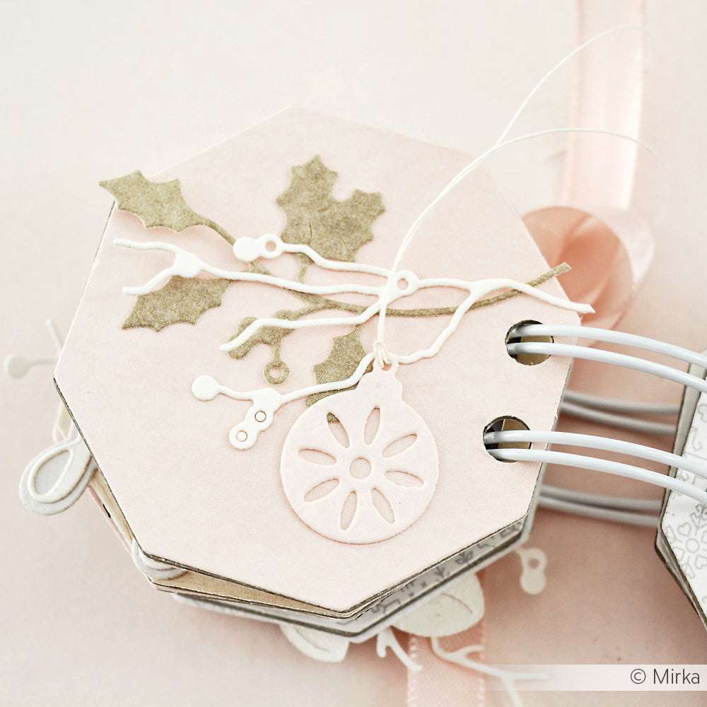 Sechseckige pastellrosa Karte von Alexandra Renke mit Stechpalmen- und Ornamentausschnitten, die mit weißen Ringen gebunden und mit Bändern verziert sind.