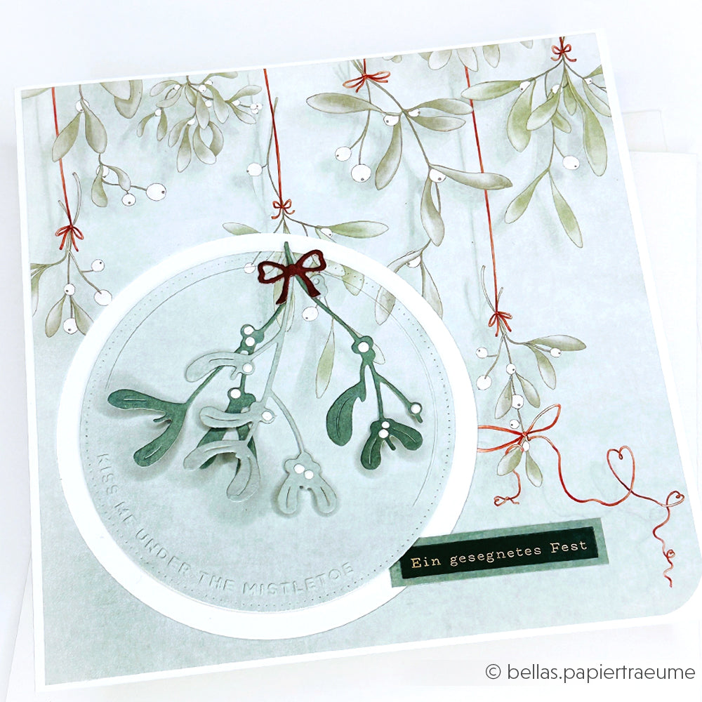 Eine Weihnachtskarte von Alexandra Renke mit einem Mistelzweig, gestanzt mit der Motivstanze Mistelzweig, verziert mit einer roten Schleife und dem Text "Ein gesegnetes Fest". Ideal für Fans von Stanzsystemen.