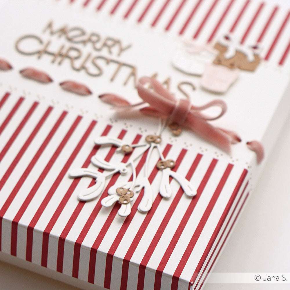 Eine gestreifte Weihnachtskarte von Alexandra Renke, verziert mit einer rosa Schleife und einem Mistelzweig unter Verwendung der Motivstanze Mistelzweig Trio, trägt die Botschaft "Frohe Weihnachten".