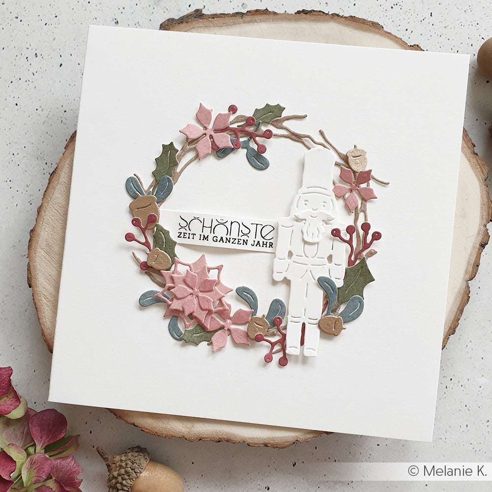 Quadratische Karte mit Blumenkranz, Nussknacker, deutschem Text und rosa, grünen und braunen Akzenten aus 200g Designpapieren - ideal für Alexandra Renke Motivstanze Weihnachtliche Blumensammlung oder Stanzen für DieCut Systeme Projekte.