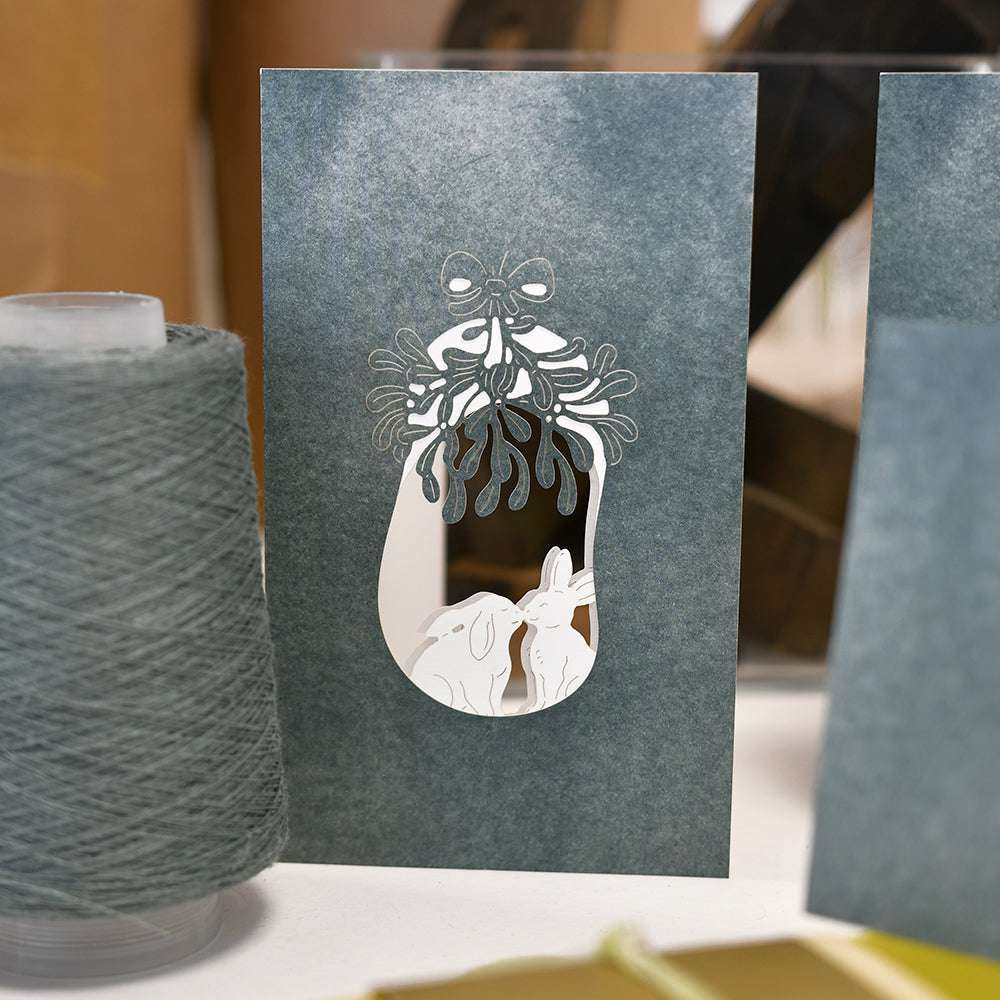 Grußkarte von Alexandra Renke mit einem weißen Ausschnitt von zwei Kaninchen unter einem Mistelzweig (Motivstanze Mistelstrauß), die auf einem Tisch aufrecht stehen sollen.