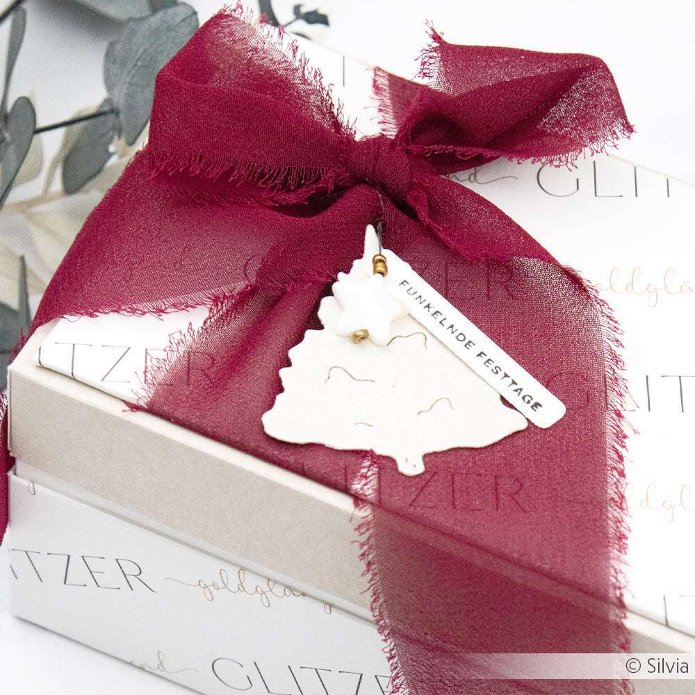 Geschenkkarton mit burgunderrotem Band und baumförmigem Anhänger, hergestellt mit der Alexandra Renke Motivstanze Tannen Trio DieCut Systeme, mit der Aufschrift FUNKELNDE FESTAGE.