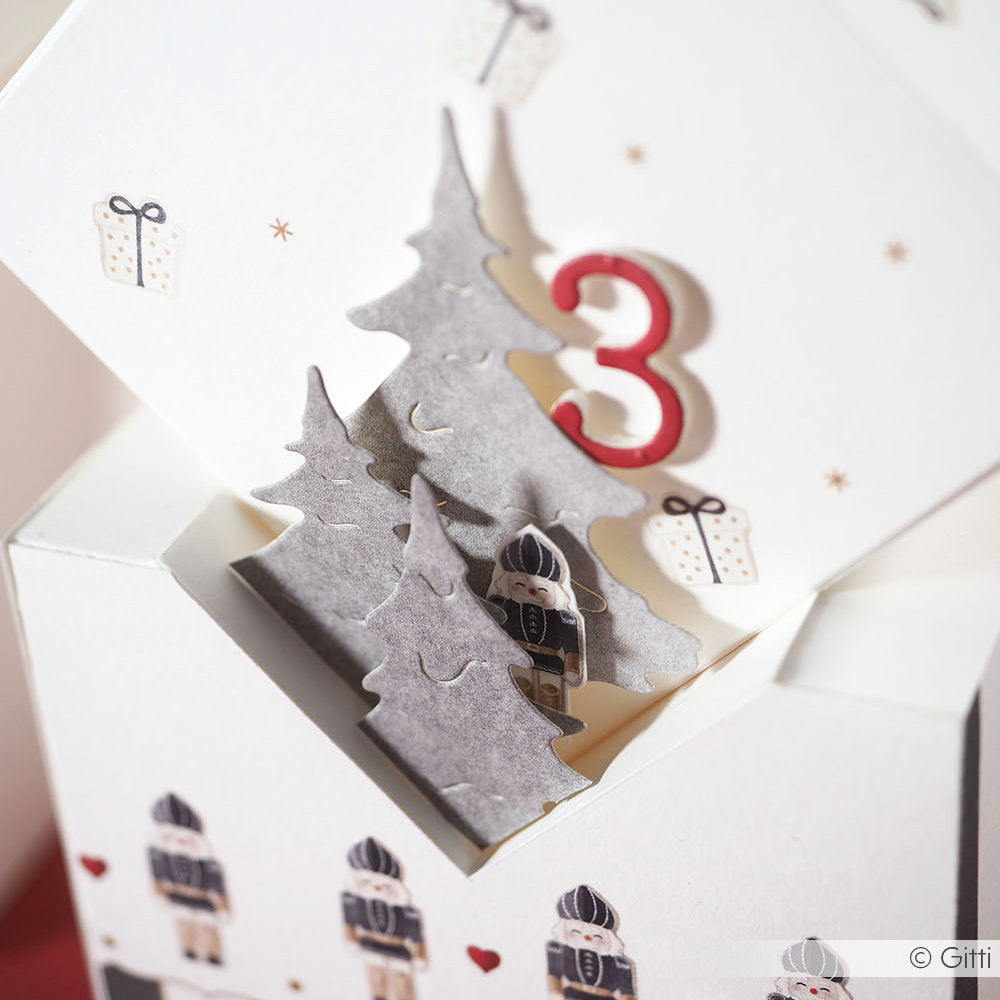 Pop-up-Karte von Alexandra Renke mit Bäumen, die mit der Motivstanze Tannen Trio geschnitten wurden, kleinen Figuren, einer roten Zahl 3 und verziert mit Geschenken und Herzen auf elegantem Designpapier.