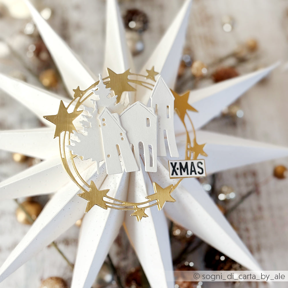 Weißes Sternenornament aus Papier mit goldenen Sternen, Häusern und Bäumen, hergestellt mit Alexandra Renke Designpapieren und DieCut Systemen, sowie einem kleinen "XMAS"-Schild in der Mitte.