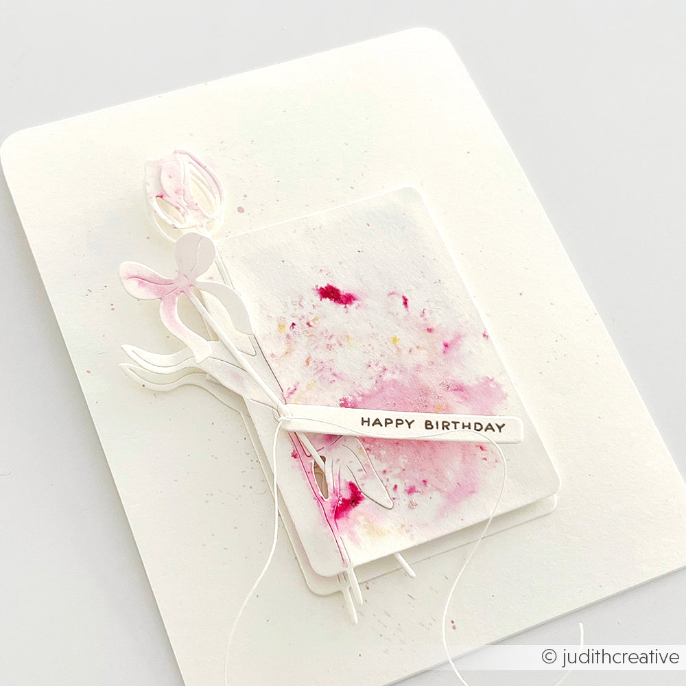 Handgemachte Geburtstagskarte von Alexandra Renke mit rosa Aquarellfarben, gestanzten Blumen mit Deep Edge Motivstanzen, Schnur und "HAPPY BIRTHDAY" Text auf weißem Hintergrund.