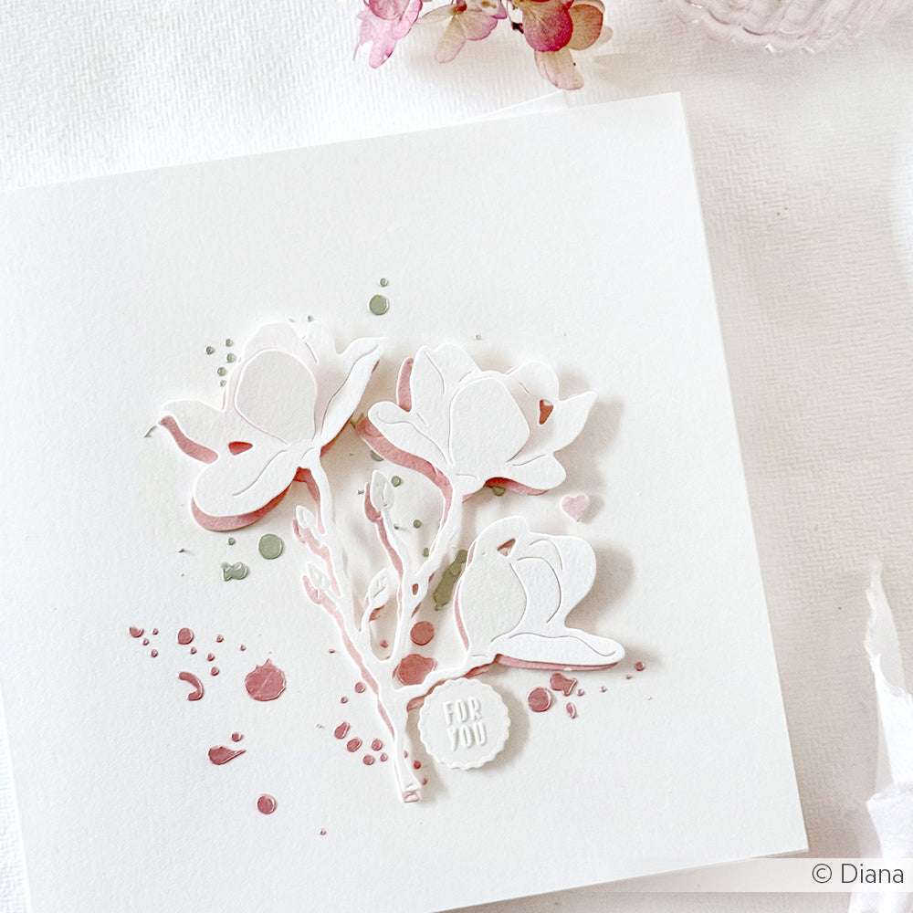 Eine weiße Karte mit drei geprägten weißen Blumen und rosa-grünen Akzenten und einem kleinen FOR YOU-Anhänger - gefertigt mit der Alexandra Renke Motivstanze Magnolienblüte für exquisite Details.