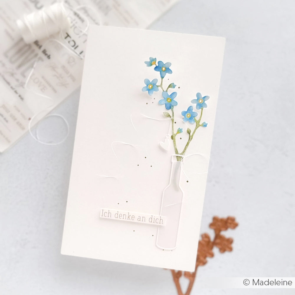 Handgefertigte Karte von Alexandra Renke mit blauen Blumen in einer Vase, erstellt mit Deep Edge Motivstanzen und Motivstanze Vergissmeinnicht, mit dem Motiv Ich denke an dich auf weißem Hintergrund.