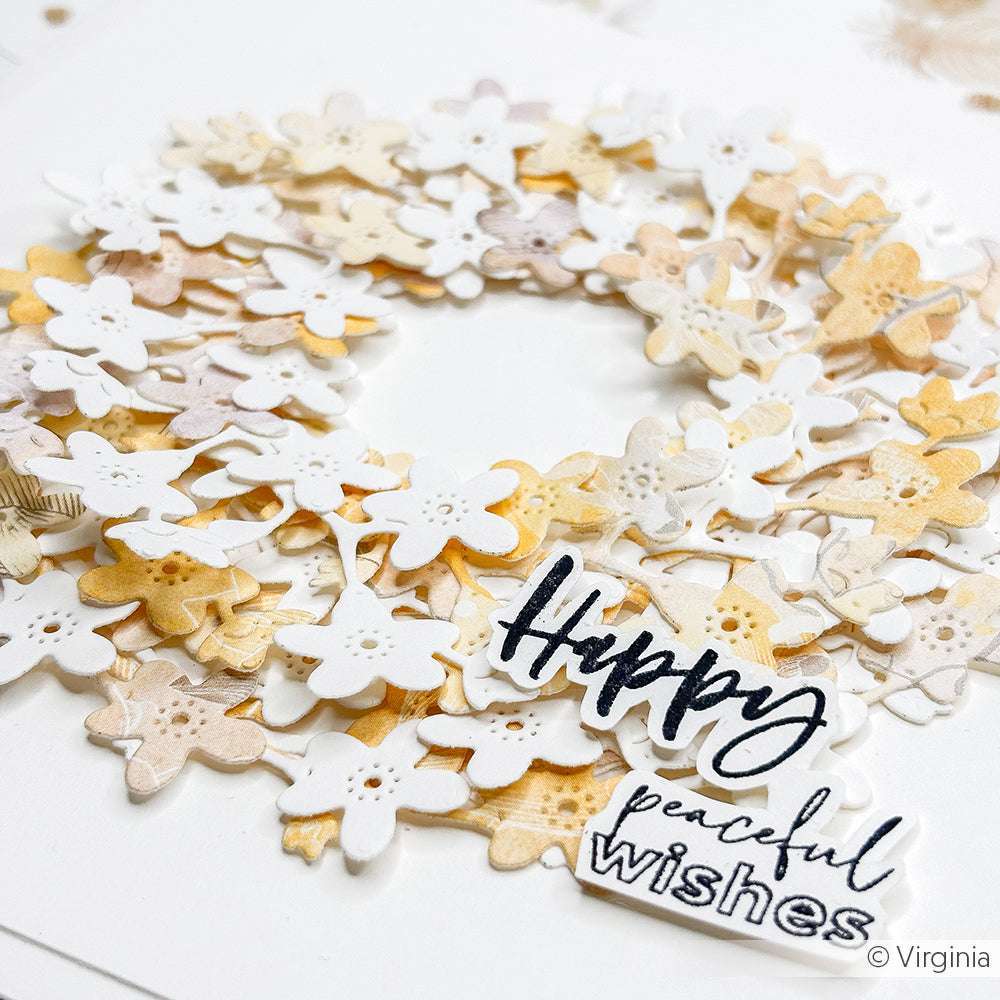 Ein Blumenkranz aus geschichteten Papierblumen von Alexandra Renke, hergestellt mit Deep Edge Motivstanzen und mit einem "Happy peaceful wishes"-Schild auf weißem Hintergrund.