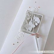 Weiße Grußkarte von Alexandra Renke mit komplizierten floralen Papierausschnitten, rosa Schnur und kleinen pastellfarbenen Perlen auf weißem Hintergrund.