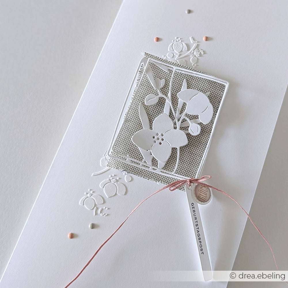 Weiße Grußkarte von Alexandra Renke mit komplizierten floralen Papierausschnitten, rosa Schnur und kleinen pastellfarbenen Perlen auf weißem Hintergrund.