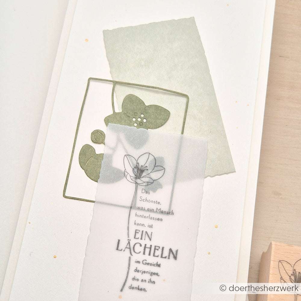 Handgefertigte Karte mit Blumenmotiven, die mit der Alexandra Renke Blumenrahmen-Stanze hergestellt wurden, durchscheinendem Overlay und deutschem Text auf hellem Hintergrund.