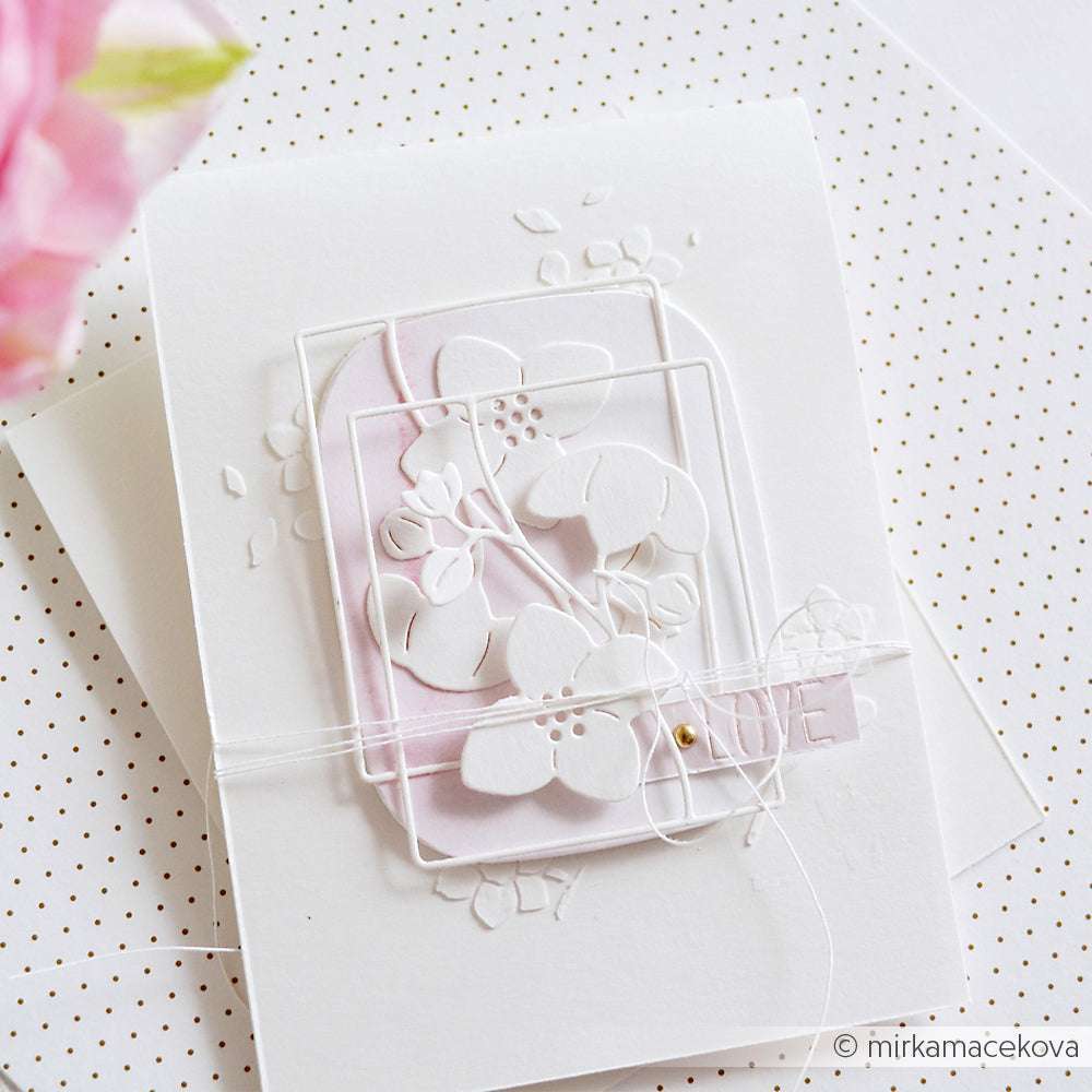 Handgemachte weiße Karte von Alexandra Renke mit geschichteten Papierblumen und Schnur auf einem gepunkteten Hintergrund, hergestellt mit Deep Edge Motivstanzen. Die rosafarbene Blume auf der linken Seite ist unscharf, um zusätzliche Dimension zu schaffen.