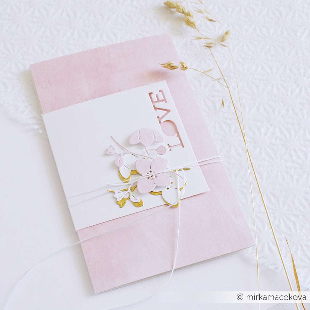 Eine rosafarbene Hochzeitseinladung mit einem Blumenausschnitt mit dem Blumenrahmen von Alexandra Renke und dem Text LOVE, verziert mit weißer Schnur und getrocknetem Gras.