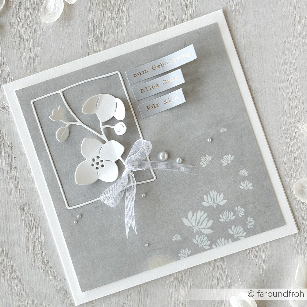 Graue florale Geburtstagskarte von Alexandra Renke mit weißen Blumen, einer Schleife und deutschem Text auf hellem Hintergrund, gestaltet mit Deep Edge Motivstanzen und veredelt mit der eleganten PAPPcut®ies Motivstanze Blumenrahmen.