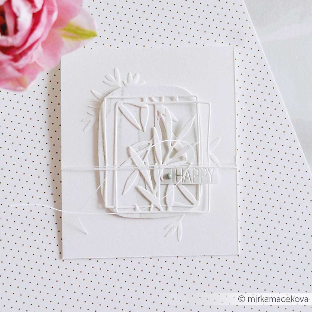 Eine weiße Grußkarte von Alexandra Renke mit geschichteten Papierausschnitten aus Deep Edge Motivstanzen, Schnur und dem Wort HAPPY. Sie wird neben einer rosa Blume gezeigt.