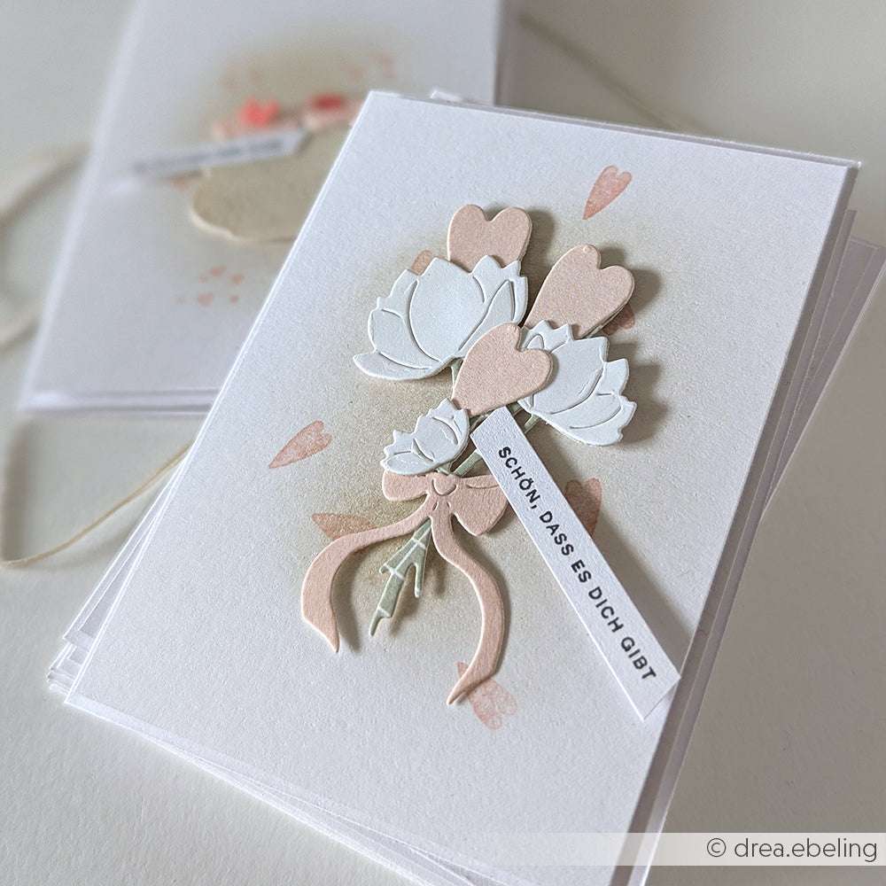 Handgefertigte Karte mit geschichteten Blumen- und Herzausschnitten, hergestellt mit Alexandra Renke Motivstanze Blumenstrauß und Deep Edge Motivstanzen, versehen mit einem Anhänger mit der Aufschrift "Schön, dass es dich gibt".