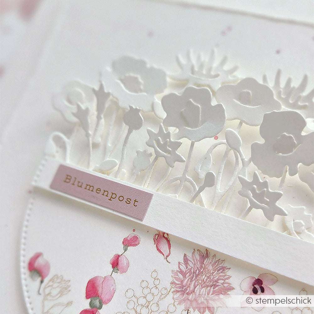 Eine blumige Grußkarte mit weißen 3D-Blumenausschnitten, die mit Alexandra Renke Motivstanze Mini Anemonen und einem Blumenpost-Etikett auf einem zartrosa Blumenhintergrund gestaltet wurde.