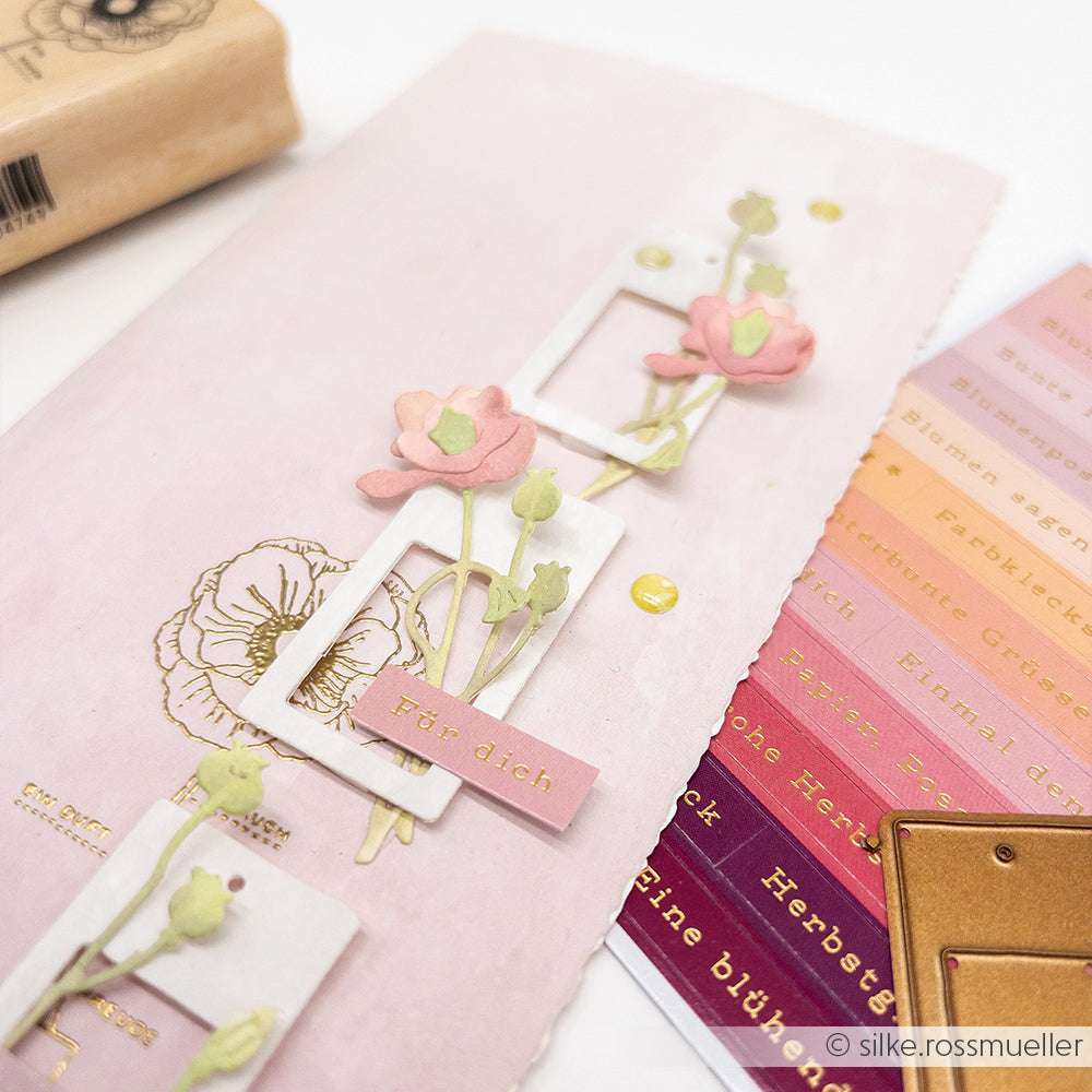 Handgefertigte Karte mit rosa Blumen, die mit der Alexandra Renke Mini Mohnblumen Stanze, goldenen Akzenten und deutschem Text auf einem zartrosa Hintergrund gestaltet wurden.