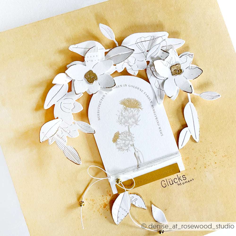 Handgemachte Karte mit weißen Papierblumen und Blättern, die mit Alexandra Renkes Motivstanze Cymbidium-Kranz auf gelbem Hintergrund mit goldenen Akzenten und Text gestaltet wurden.