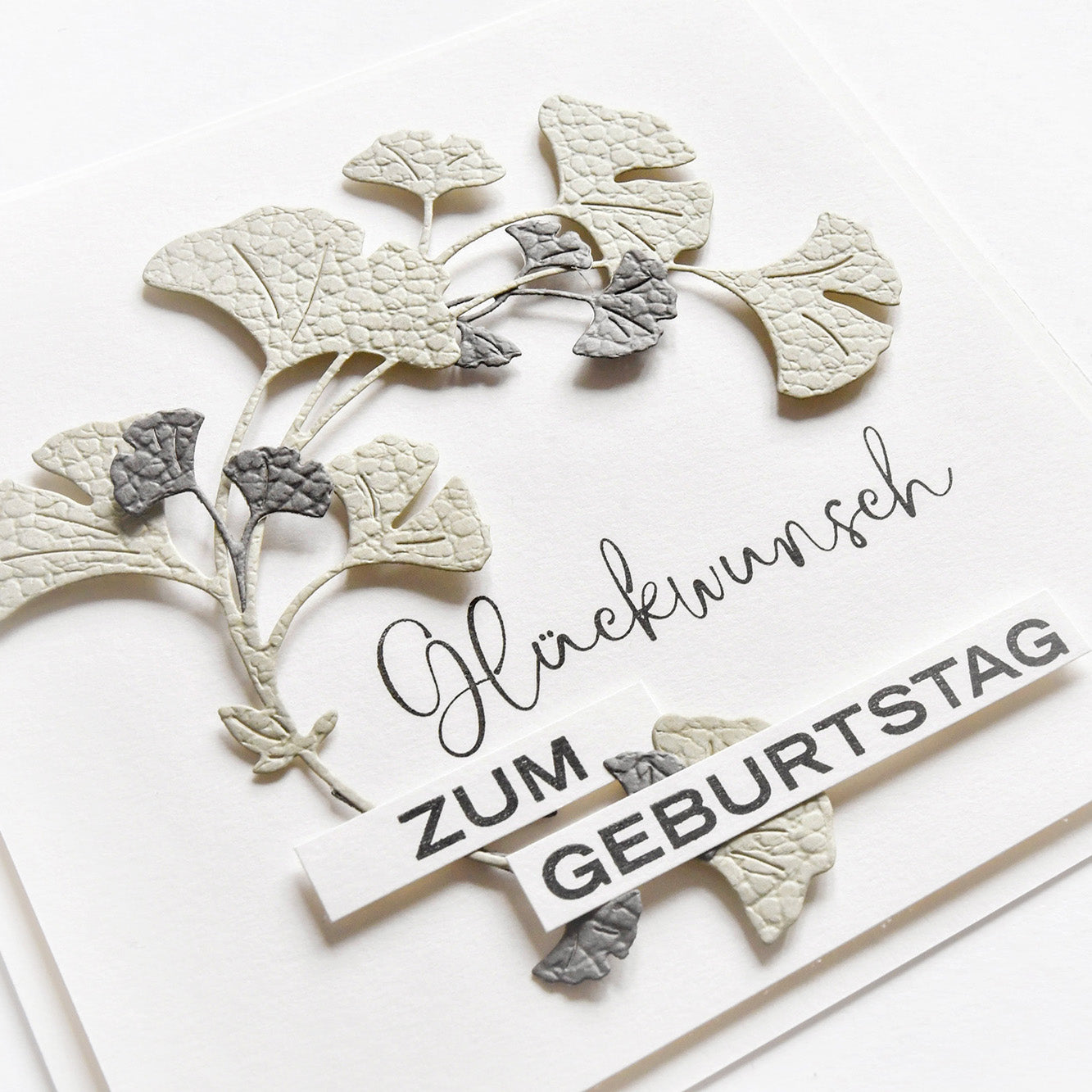 Eine handgefertigte Karte von Alexandra Renke mit geprägten Ginkgoblättern, hergestellt mit der Ginkgo-Kranz Motivstanze und verziert mit dem deutschen Text "Glückwunsch zum Geburtstag".